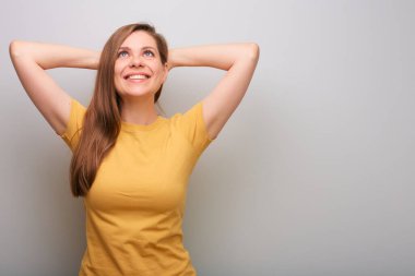 Elleri başının arkasında yukarı bakan mutlu bir kadın. Gri duvar arka planında izole edilmiş kadın portresi.