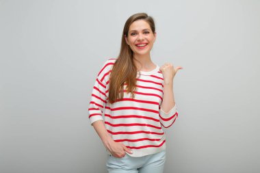 Gülümseyen kadın başparmağıyla işaret ediyor, izole edilmiş stüdyo resmi, kırmızı çizgili beyaz kazaklı kız...