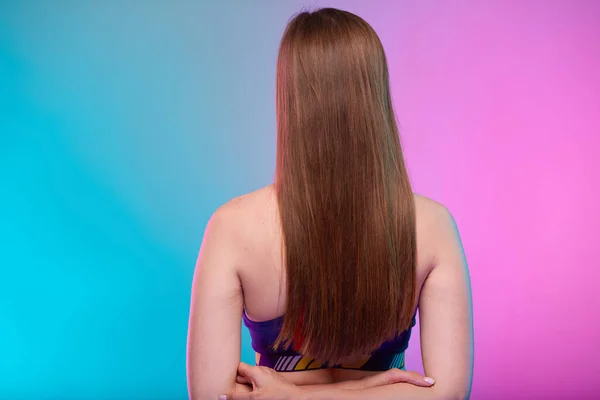 フィットネスで長い髪を持つスポーティ女性は 背後に手でバックビューを誓う ネオン多色の背景に隔離された女性フィットネスの肖像画 — ストック写真