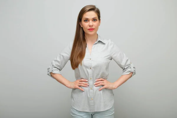 Smiling confident woman standing with hands on hips, isolated female portrait, young lady dressed pants and gray shirt.