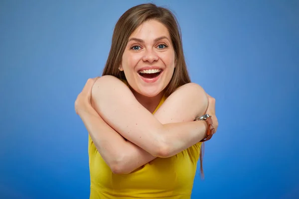 Woman smiling and hugging herself. Isolated female portrait on blue background.