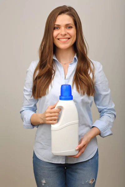 Woman in casual clothes blue shirt and jeans holding laundry detergent in white big bottle.