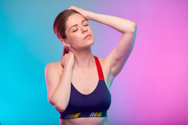 Başı ağrıyan bir kadın gözleri kapalı kafasına dokunuyor. Spor giyimli kız. Neon mavisi arka planda izole edilmiş kadın fitness portresi.