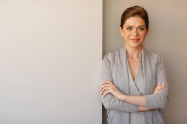 Kollarını kavuşturmuş bir iş kadını. Gri iş elbisesi içinde gülümseyen kız..