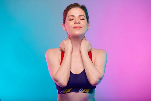 Smiling relaxing woman with closed eyes in fitness bra sportswear holding hands behind neck. Female fitness portrait isolated on neon color background.