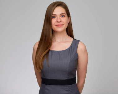 Gri elbiseli gülümseyen kadın ellerini arkasında tutuyor. Gri üzerine izole edilmiş stüdyo resmi. 