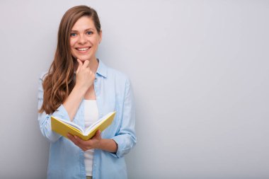 Gülümseyen kadın öğretmen ya da öğrenci açık bir kitap tutuyor ve çenesine dokunuyor.  