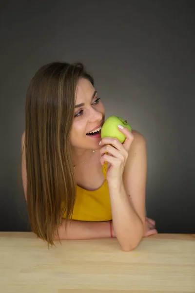 女性はテーブルに座って緑のリンゴをかむ 離れて見て 天然の女性像 — ストック写真