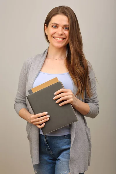 Smiling student with long hair dressed casual holding book,  isolated portrait on gray.