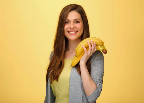 Smiling woman holding bananas fruits isolated on yellow studio back.