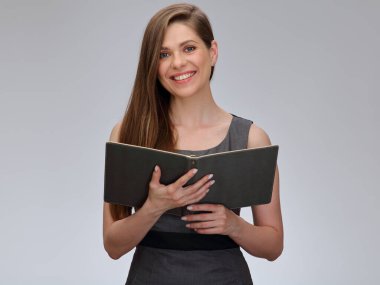 Gülümseyen öğretmen ya da gri iş elbiseli öğrenci kadın açık bir kitabın önünde duruyor, izole edilmiş bir portre..