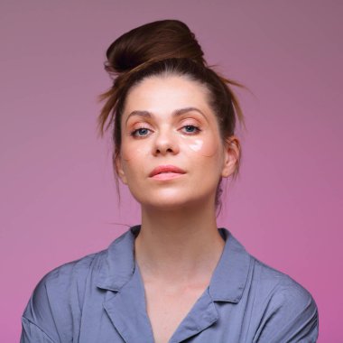 Genç kadın pijaması giyinmiş, pembe kadın yüz portresi üzerinde izole edilmiş göz bantları ve çörek saç stiliyle..