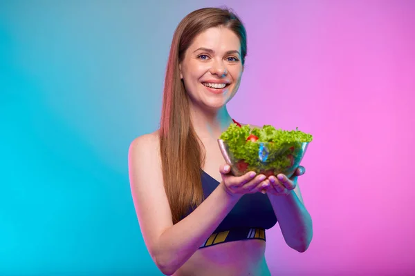 フィットネススポーツウェアを着たスポーティな女性の笑顔緑色のサラダとガラスボウルを保持ネオンマルチカラーの背景に隔離された女性のフィットネスの肖像画 健康食品 — ストック写真