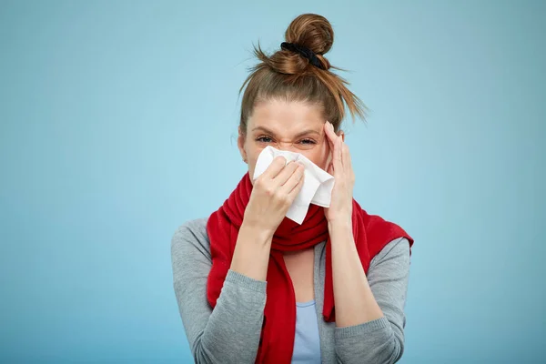 Sick woman with cold caught sneezing into tissue. Sick woman with headache isolated portrait with red scarf on light blue back.