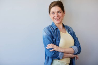 Yanlız bir kadın gülümsüyor ve kolları çapraz duruyor, mavi gömlekli, başka tarafa bakıyor..