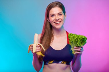 Gülümseyen mutlu kadın elinde salata ve muz tutuyordu. Neon renkli arka planda sağlıklı yiyeceklerle izole edilmiş kadın fitness portresi..