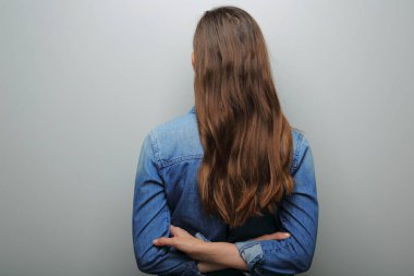 Uzun saçlı kadın arkada duruyor. Gri duvarda izole edilmiş bir portre var.. 