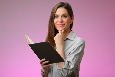 Gülümseyen öğretmen kadın açık bir kitap tutuyor ve çenesine dokunuyor, pembe üzerine izole edilmiş bir portre..