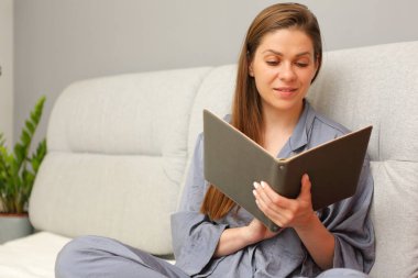 Dinlenen kadın yatakta oturup kitap okuyor..