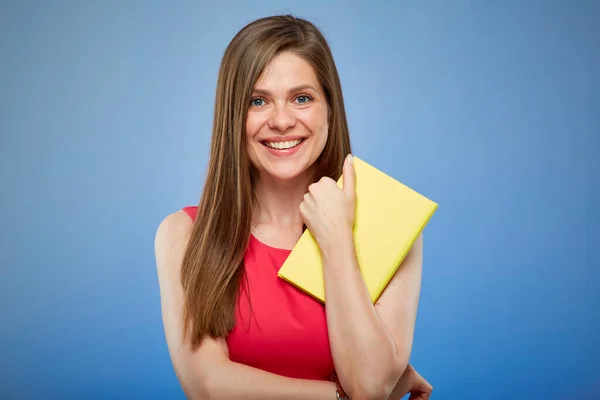 Student lady in red dress holding yellow book, isolated portrait on blue background.