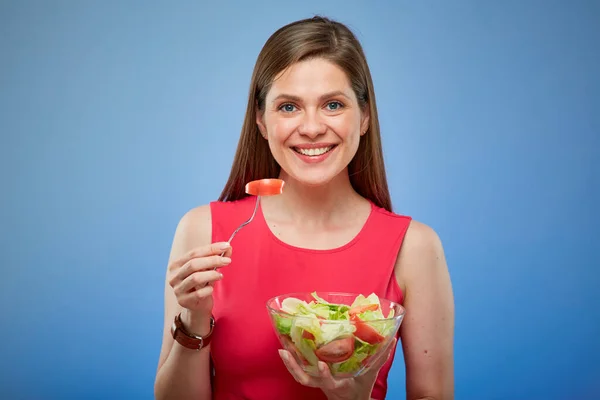 緑のサラダをフォークで食べる赤いドレスの若い女性 青い背景の孤立した女性の肖像画 — ストック写真