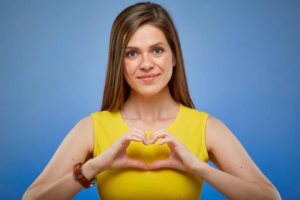 Woman smiling and doing heart gesture with fingers. Isolated female portrait on blue background.