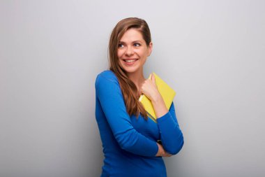 Kitabı olan öğrenci kadın, gri duvarın yanındaki izole edilmiş portreye bakıyor..