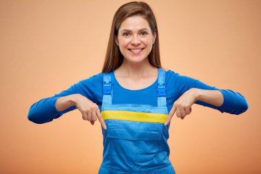 Gülümseyen bir kadın işçi ya da mavi tulumlu bir öğrenci parmaklarını aşağı işaret ediyor. İzole edilmiş kadın portresi.