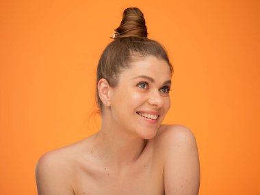 Çıplak omuzlu gülümseyen bir kadın, saçı topuz gibi, bakışlarını kaçıran, güzellik tarzında izole edilmiş bir portre, doğal bir yüz portresi, rötuş yapmadan..