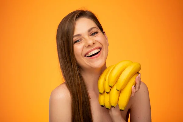 Smaling woman face portrait, girl holding banana bunch isolated portrait on yellow orange background.