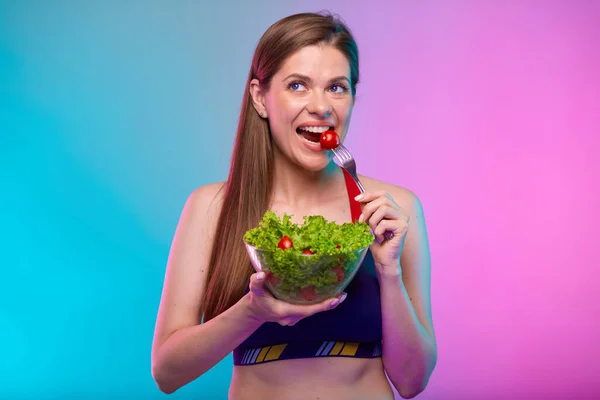 スポーツウェアの女がトマトをグラスボウルに入れてグリーンサラダを食べる ネオン多色の背景に隔離された女性フィットネスの肖像画 — ストック写真