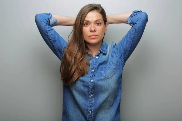 Serious woman in blue casual denim shirt with hands behind her neck. isolated female portrait.