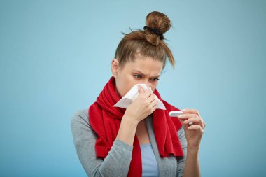 Soğuk algınlığına yakalanmış hasta bir kadın. Dokuya hapşırıyorum. Baş ağrısı olan hasta bir kadın açık mavi üzerine izole edilmiş bir portre..