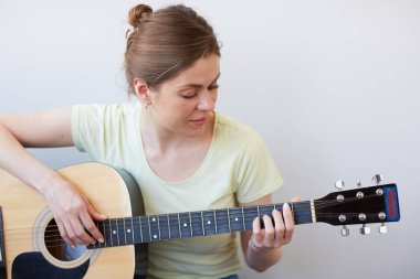 Gülümseyen kadın gitarla oynar ve aşağı bakar. Gri sırtlı izole edilmiş portre.