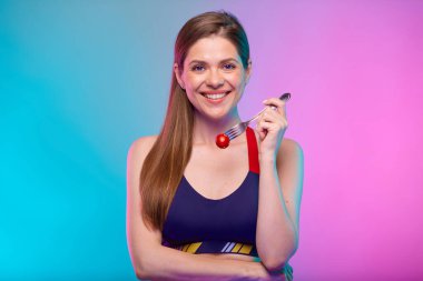 Spor sutyenli, çatallı kırmızı domatesli gülümseyen bir kadın. Neon arkaplanda izole edilmiş kadın fitness portresi.