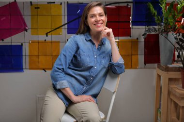 Gülümseyen kadın tasarımcı sınıfta renk paletiyle oturuyor..