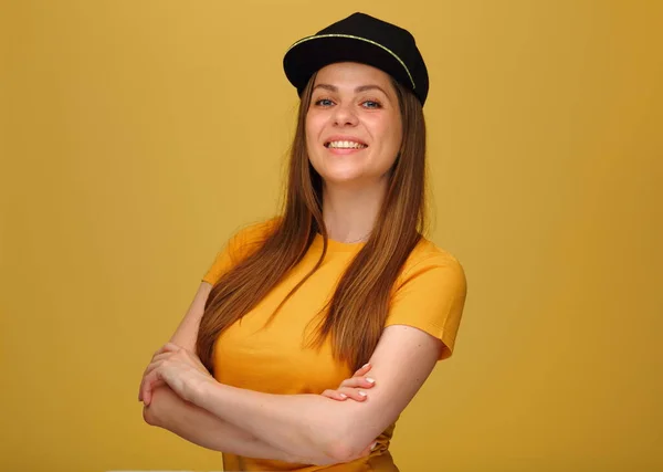 Happy woman in yellow shirt with black cap standing with crossed arms isolated on yellow.