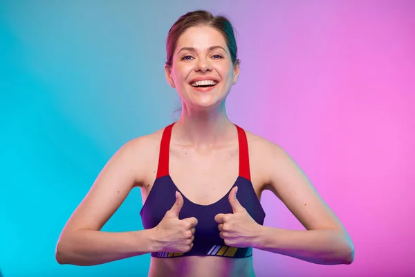 身披运动胸罩 笑容可亲的女人戴着两个大拇指 女性健身肖像孤立在霓虹灯的色彩背景上 瑜伽教师的健康生活方式概念 — 图库照片