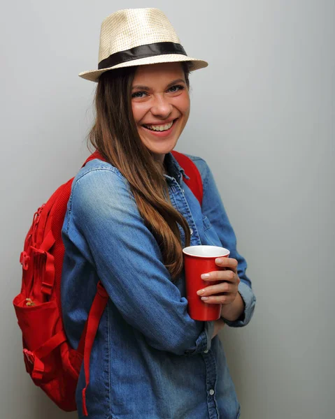 コーヒーグラスで夏の帽子隔離された肖像画を身に着けている笑顔の女性学生 レッドバックパック ブルーデニムシャツ — ストック写真