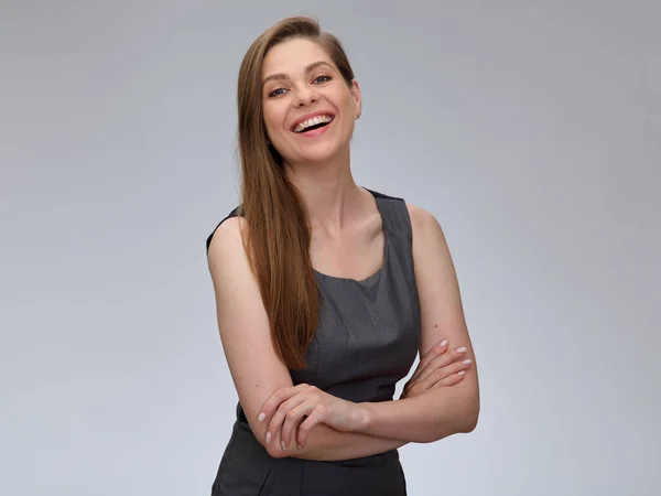 Laughing business woman wearing gray dress standing with arms crossed isolated portrait.