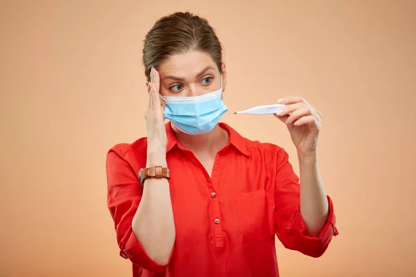 Sick woman with medical mask looking on digital thermometer, isolated female portrait. Girl in red shirt.