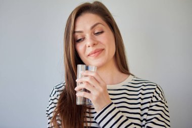 Genç bir kadının su bardağını tutarken ve aşağıya bakarken yakın plan fotoğrafını çek. Çizgili tişörtlü gülümseyen kızın izole edilmiş portresi.