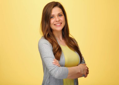 Kollarını kavuşturmuş gülümseyen bir kadın. Sarı arka planda izole edilmiş kadın portresi.