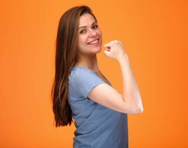 Gülümseyen mavi gömlekli genç kadın boynuna dokundu ve turuncu arka planda izole edilmiş portreye baktı..