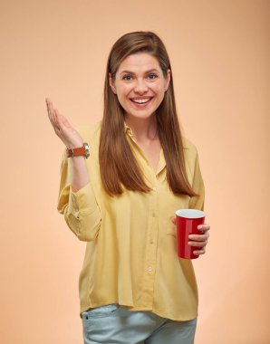 Gülümseyen kadın hareketi, sarı arka planda izole edilmiş bir portre. Uzun saçlı genç bayan elinde kırmızı kahve fincanı tutuyor..