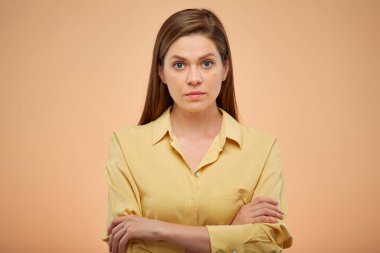 Stüdyo sarı arka planda kollarını kavuşturmuş ciddi bir kadın..
