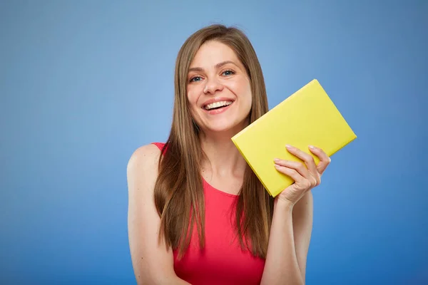 Smiling student woman in red dress holding yellow book  Isolated female person portrait on blue background.
