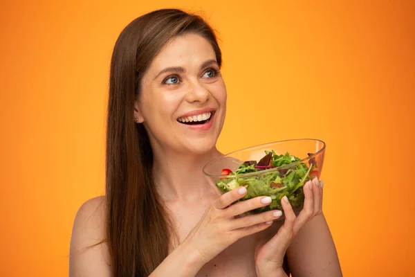 笑容满面的女人 赤裸裸的肩膀 把绿色的沙拉放在玻璃碗里 把孤立的肖像放在橙色的黄色背景上看去 — 图库照片
