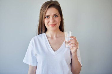 Beyaz gömlek giyen bir kızın izole edilmiş portresi. Uzun saçlı, sırıtan genç bir kadın su bardağı tutuyor.. 