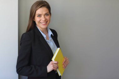 Siyah takım elbiseli kadın öğretmen gülümsüyor. Öğrenci kız ya da iş kadını sarı kitap tutuyor.